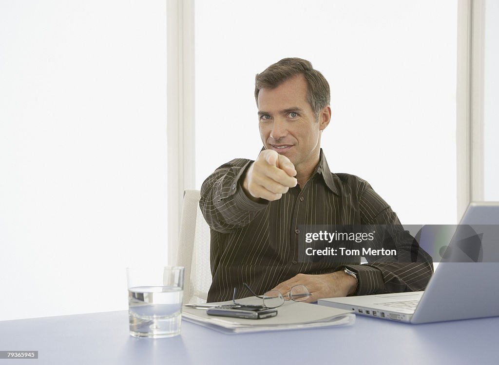 Businessman in boardroom pointing at camera