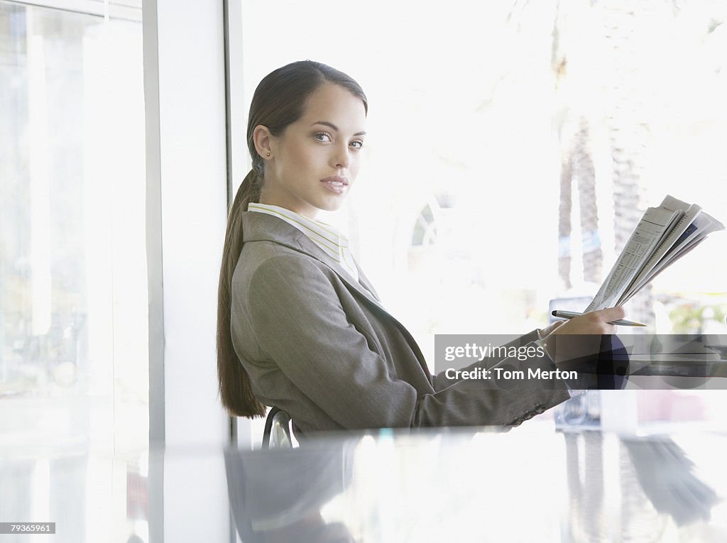 Businesswoman sitting on outdoor patio with newspaper