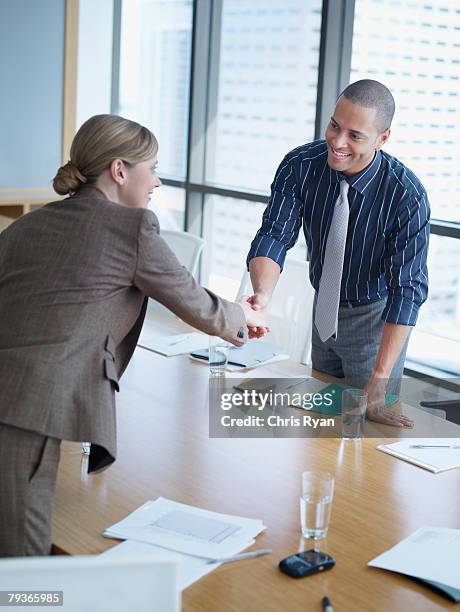 two businesspeople in boardroom shaking hands - woman-man-handshake-across-table stock pictures, royalty-free photos & images