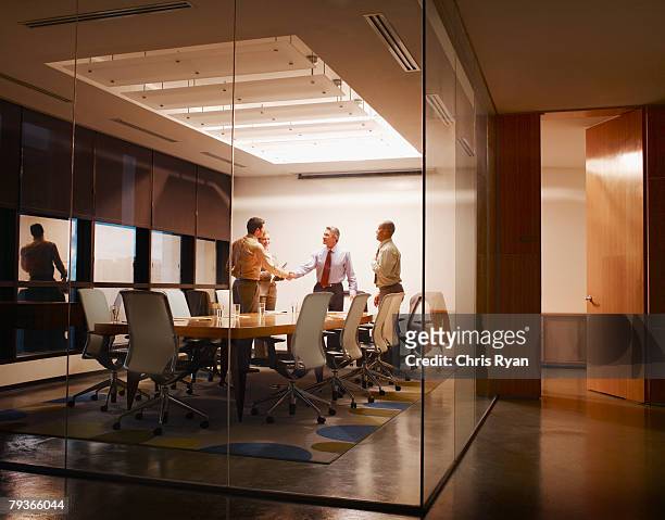 four businesspeople in boardroom with two shaking hands - board room stock pictures, royalty-free photos & images