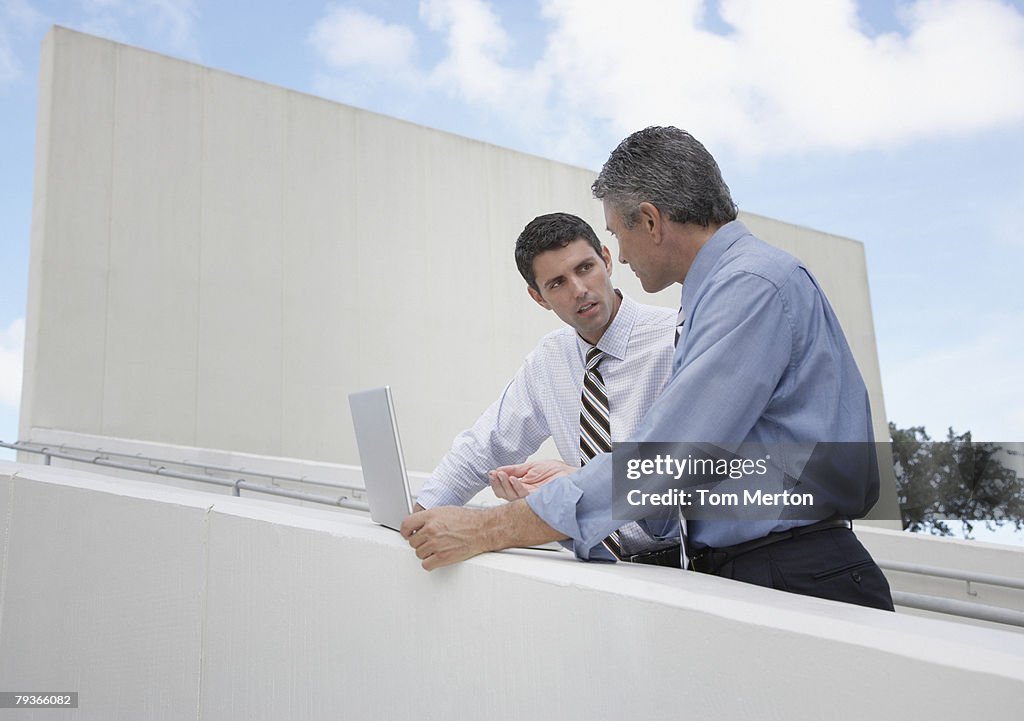 Two businessmen on an outdoor staircase with a laptop