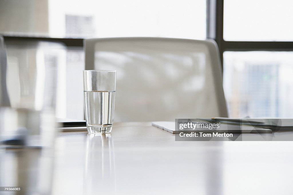 Empty boardroom chair with notepads and glasses of water on table