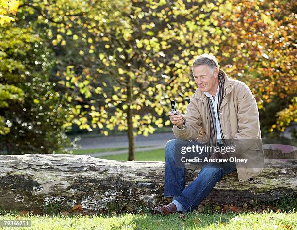 man outdoors sitting on a large log looking at his mobile phone - andrea park stock pictures, royalty-free photos & images