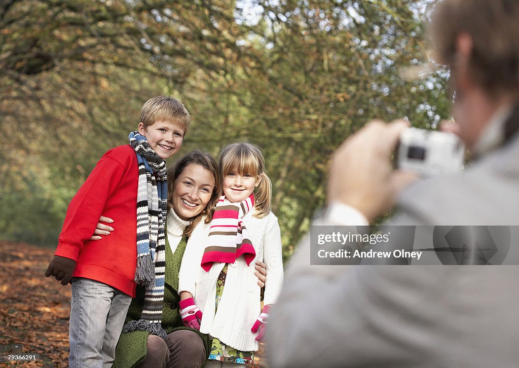 Man outdoors taking a picture of woman and two young children with a digital camera