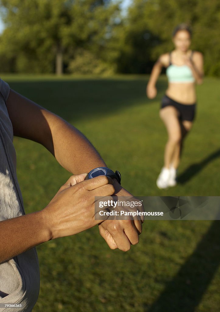 Woman running in a park outdoors while a man times her
