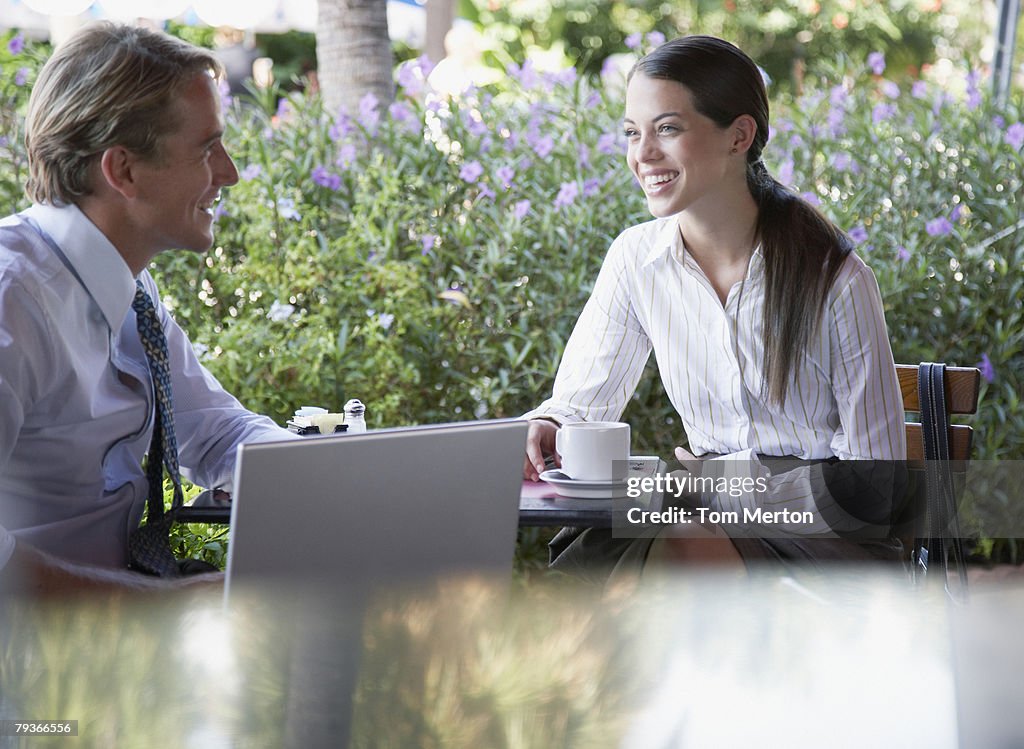 Businessman and businesswoman sitting at a patio table with laptop