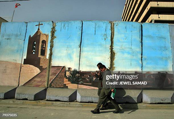 Iraqi men walk past a painted concrete blast wall securing an office building in downtown in Baghdad, 30 January 2007. Violence has surged in the...