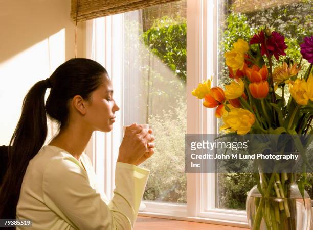 mixed race woman relaxing next to window - mixed race woman drinking tea stock-fotos und bilder