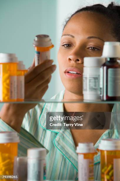 african american woman looking at medication bottle - armoire de toilette photos et images de collection