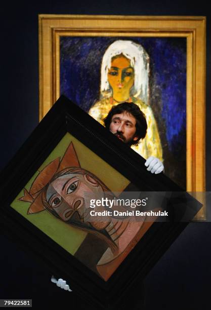 In this photo illustration a Christies employee holds Pablo Picasso's Femme Au Chapeau as Kees Van Dongen's, L'ouled Nail hangs behind during a press...