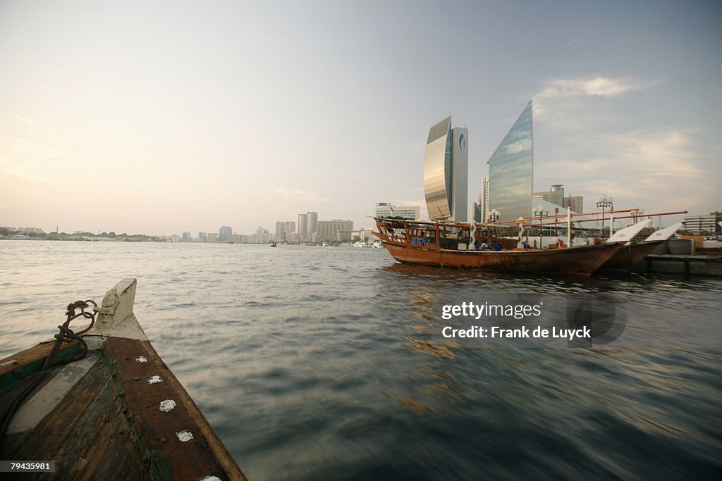 Dubai skyline photographed from an abra sailing in Dubai Creek. Traditional dhows can be seen moored alongside quays. Dubai Creek, Dubai, United Arab Emirates