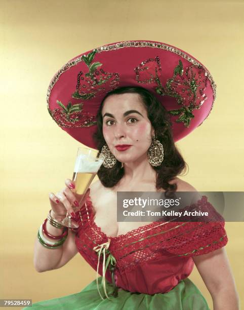 Portrait of model Esther Fernandez as she poses in a sombrero, an low-cut blouse, and oversize earrings with a tall glass of beer in her hand, July...