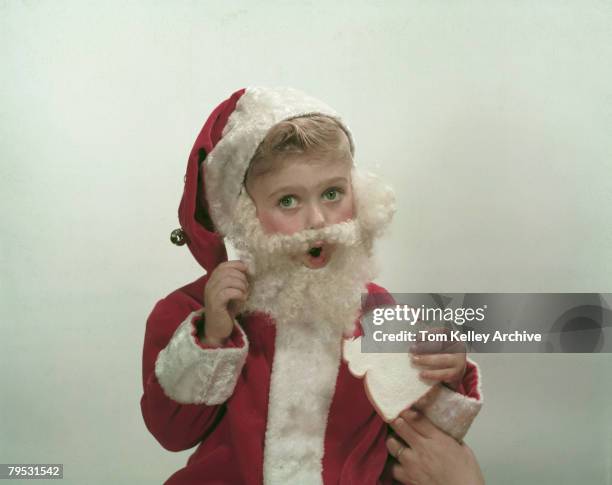 Portrait of child model Bryan Cuthill, dressed in a Santa Claus costume, as he eats a piece of white bread, June 7, 1957. A hand is visible the the...