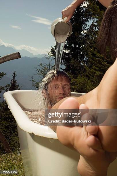 young man lying in bathtub, young woman pouring water on man's head - wellness kindness love stock pictures, royalty-free photos & images