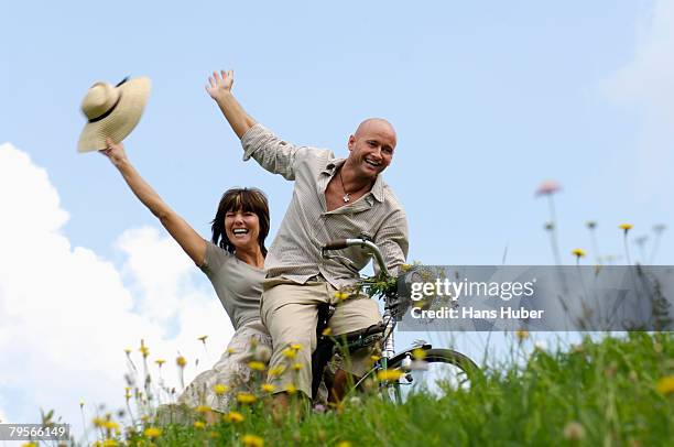 couple riding bicycle in meadow - partnership men bikes stockfoto's en -beelden