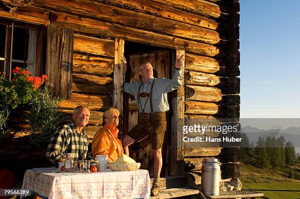 mature couple sitting in front of alpine hut, talking to farmer - alm hütte stock-fotos und bilder