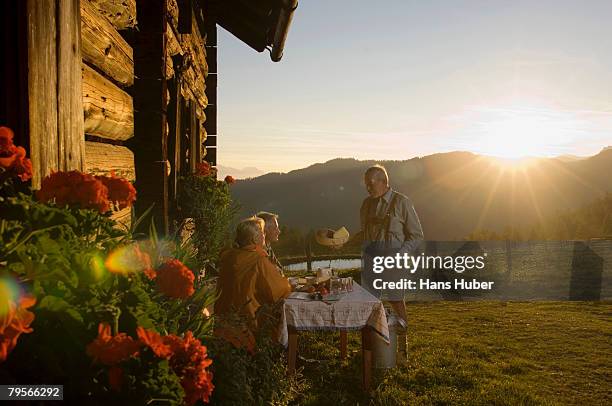 farmer serving mature couple sitting in front of alpine hut - mangiare natura foto e immagini stock