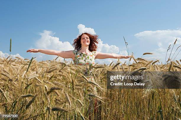 young woman standing in cornfield, arms outstretched, smiling - arm span stockfoto's en -beelden