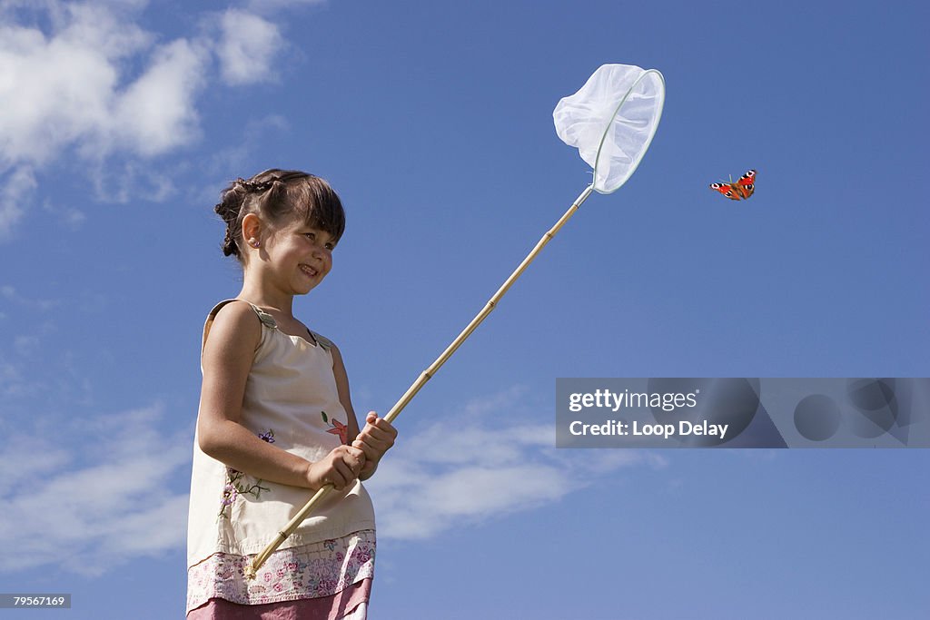 Girl (7-9) holding net, trying to catch butterfly