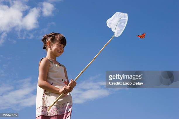 girl (7-9) holding net, trying to catch butterfly - catching butterfly stock pictures, royalty-free photos & images