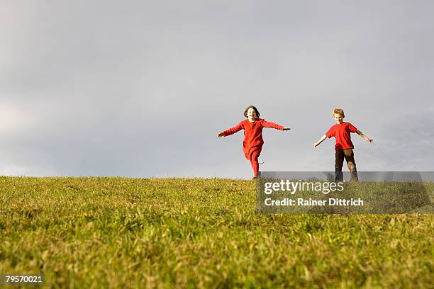 boy (10-12) and girl (7-9) running in meadow arms outstretched - preadolescent kind 個照片及圖片檔