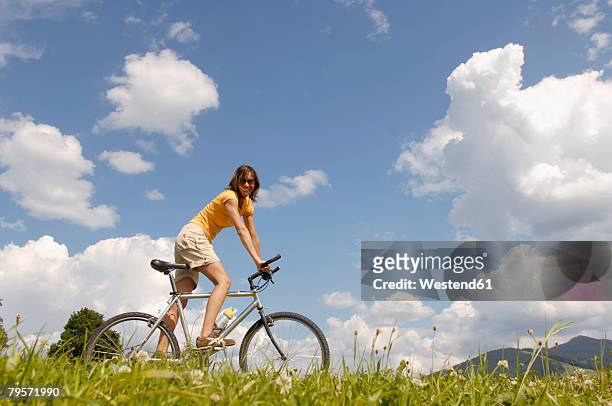 young woman riding bicycle in meadow, side view - porträt frau blick in ferne stock-fotos und bilder