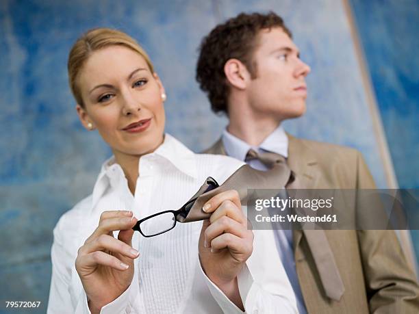 business woman cleaning spectacles with man´s tie - tyranny stockfoto's en -beelden