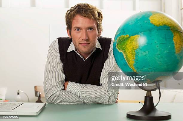young man sitting on desk, globe in foreground - globe businessman stockfoto's en -beelden