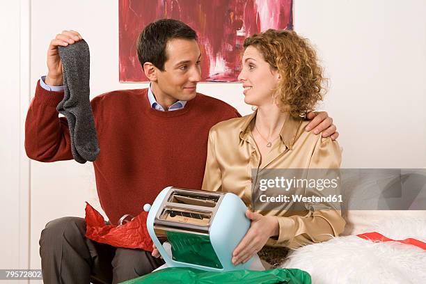 couple sitting on sofa, holding toaster and socks - male female pair stockfoto's en -beelden