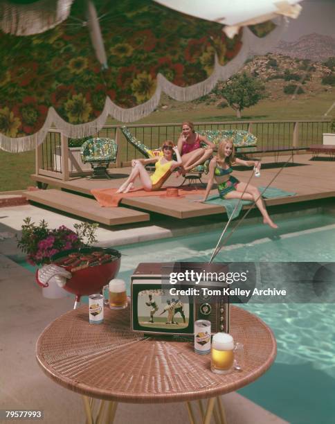 Three woman in swimwear relax at a poolside, while in the foreground, a portable television set shows a baseball game, 1967. The photo was taken as...