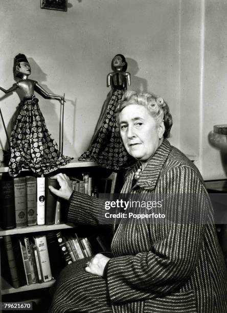 English writer and novelist Agatha Christie seated reading by a bookshelf of books in a living room at her home, Winterbrook House near Wallingford,...