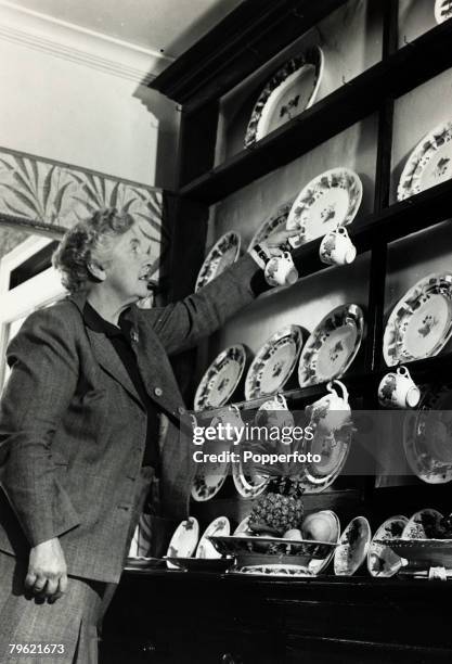 English writer and novelist Agatha Christie reaches for a china plate on a Welsh dresser in the dining room of her home, Winterbrook House near...