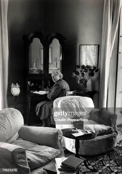 English writer and novelist Agatha Christie seated at a writing desk in a living room in her home, Winterbrook House near Wallingford, Oxfordshire in...