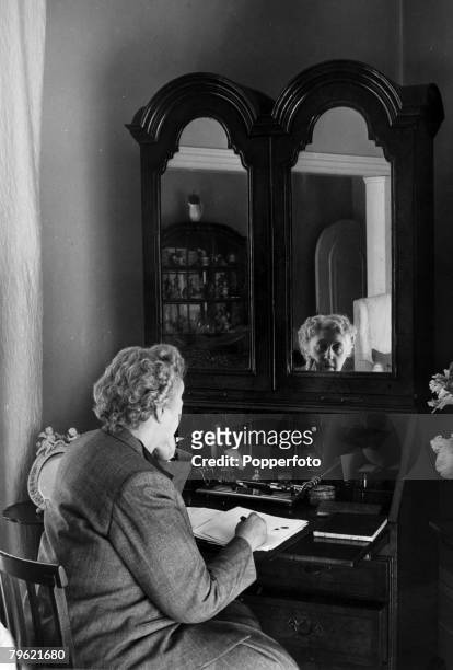 English writer and novelist Agatha Christie seated at a writing desk in a living room in her home, Winterbrook House near Wallingford, Oxfordshire in...