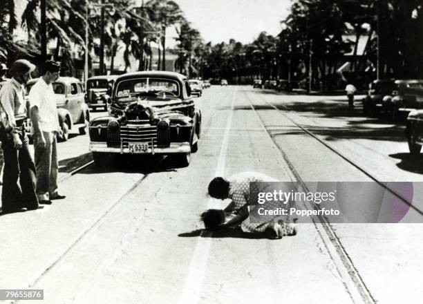 Hawaiian mother bends over her little daughter, struck by a frantic motorist during the panic caused by the Japanese attack on Pearl Harbour, Hawaii,...