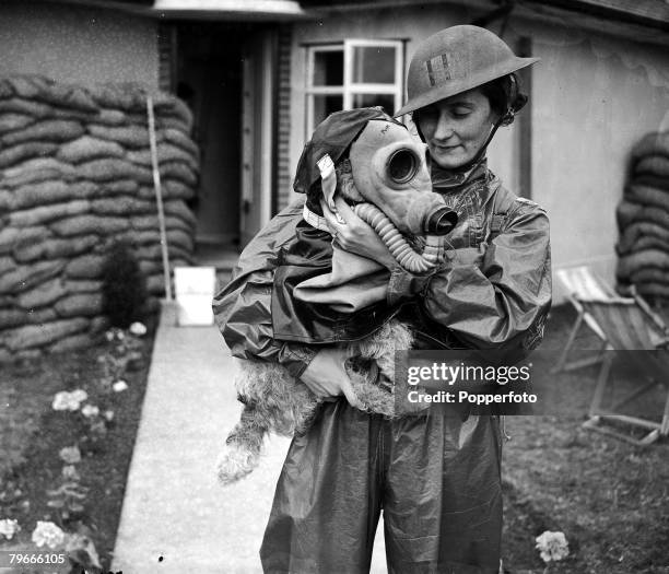 28th July 1938, Chatham, Kent, A woman member of the Gillingham, Kent Air Raid Precautions First Aid Squad cuddles a dog fitted with a gas mask...