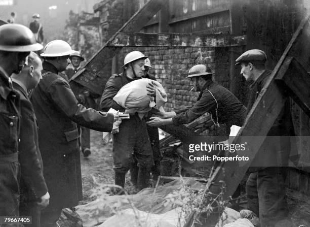 World War II, 10th October 1940, A stretcher party member carrying the body of a 12 month old baby past the wreckage of an air raid shelter in London...