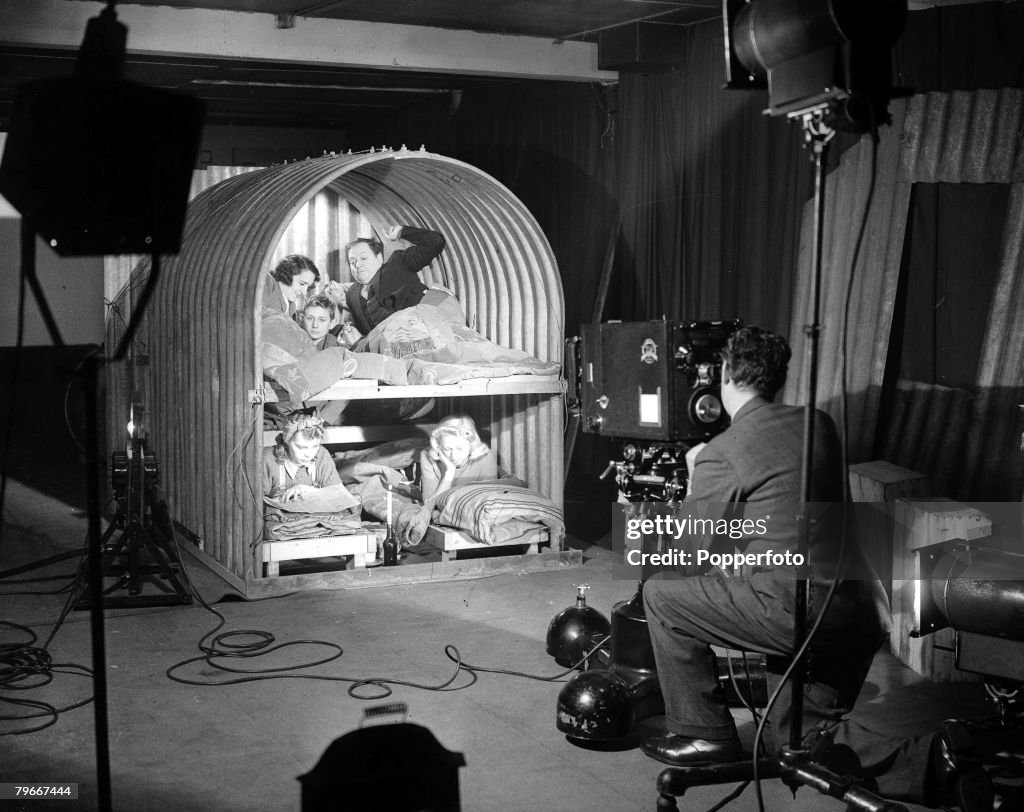 England, 1940, A studio picture showing a cameraman filming a typical wartime family inside their Anderson bunk shelter to protect them from falling bombs in Nazi german air raids during World War Two