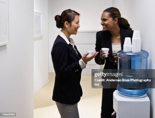 multi-ethnic businesswomen talking at water cooler - trinkwasserbehälter stock-fotos und bilder