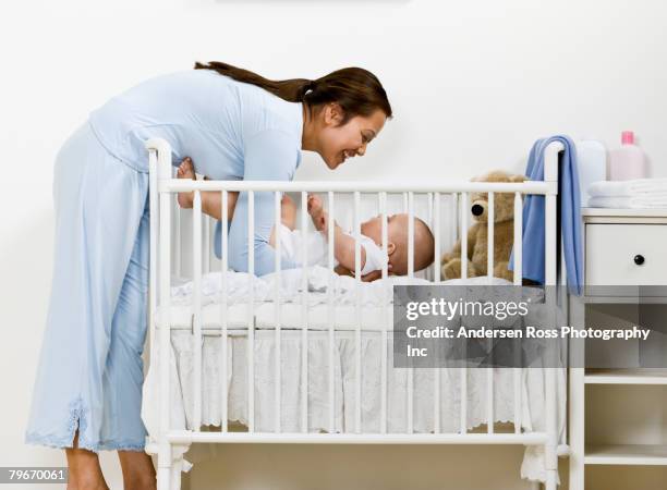 asian mother laying baby in crib - eltern baby hochheben stock-fotos und bilder