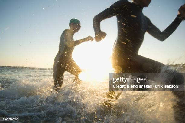 multi-ethnic swimmers running in surf - swimming race imagens e fotografias de stock