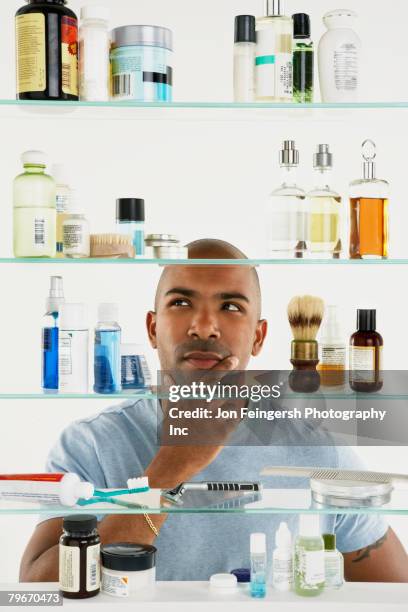 african american man looking in medicine cabinet - badezimmerschrank stock-fotos und bilder