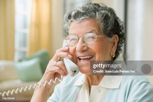 senior hispanic woman talking on cell phone - landline phone home foto e immagini stock