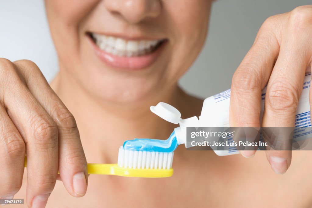 Hispanic woman putting toothpaste on toothbrush