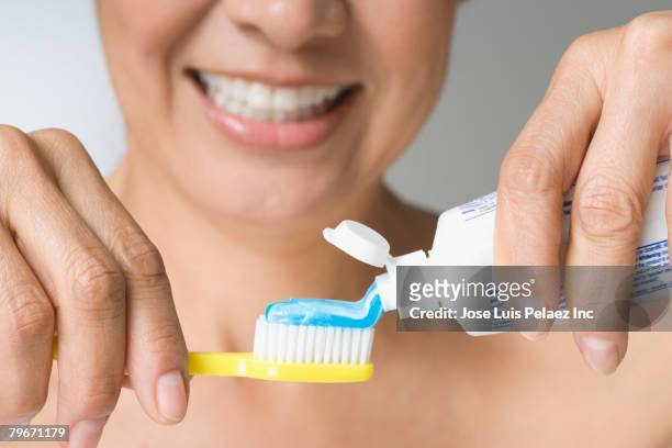 hispanic woman putting toothpaste on toothbrush - toothpaste imagens e fotografias de stock
