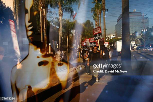 Writers Guild of America members and supporters are reflected in a bus stop ad for the Oscars awards show while picketing in front of NBC studios as...