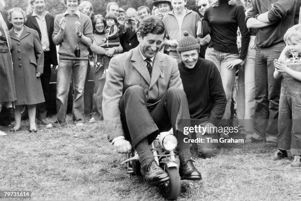 Prince Charles, Prince of Wales riding a mini motorbike at Bisley Rifle Range