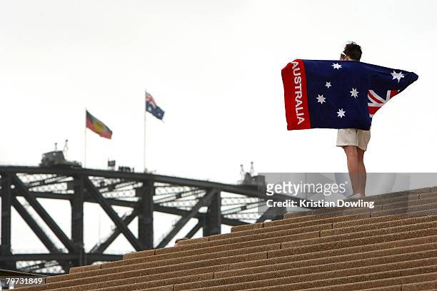 Woman stands on the steps of the Sydney Opera House looking out to the Aboriginal and Australian flags flying on the Sydney Harbour Bridge on the day...