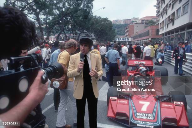 Racing driver Jackie Stewart makes a television broadcast at the Monaco Grand Prix, 22nd May 1977. Behind him is John Watson's 'Martini' race car.