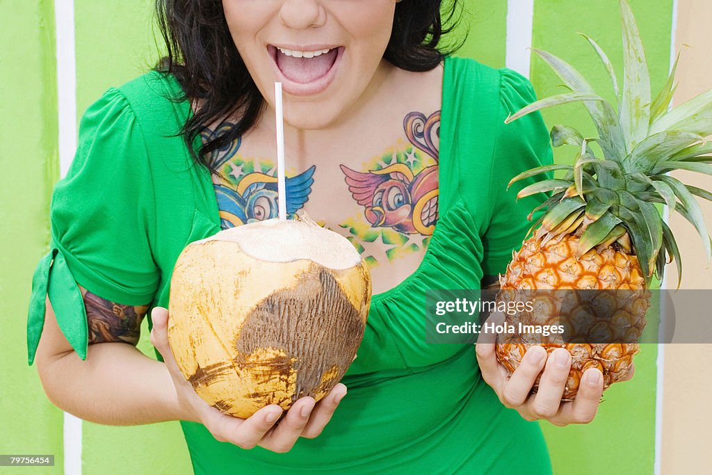 Mid section view of a young woman holding a pineapple and drinking coconut milk with a drinking straw